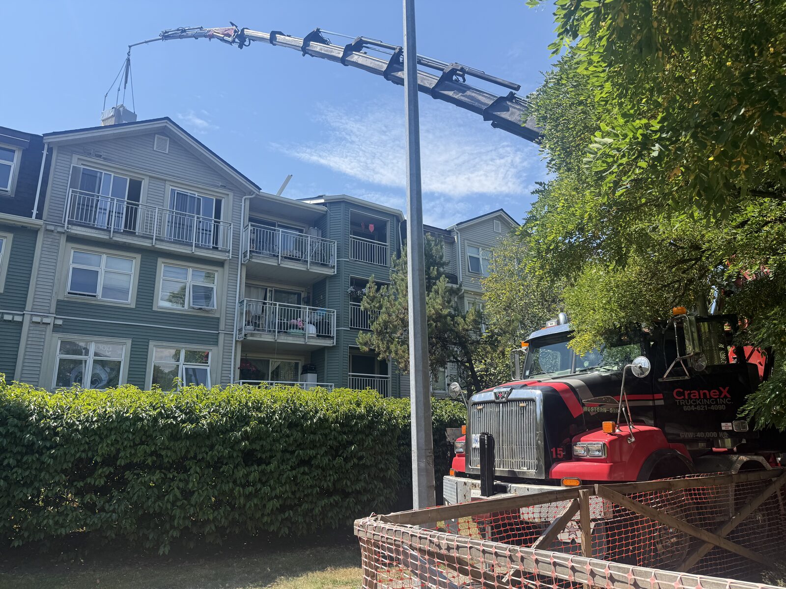 CraneX knuckle boom crane lifting a rooftop HVAC unit over a building